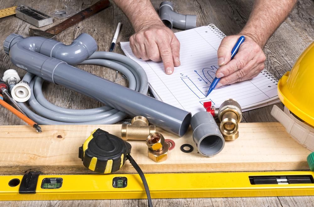 A Man Is Drawing a Pipe on A Piece of Paper — Coffs Coast Plumbing in Korora, NSW