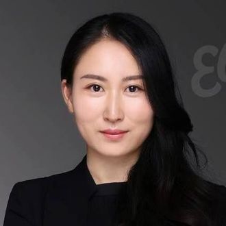 A woman with long black hair is wearing a black jacket and looking at the camera.
