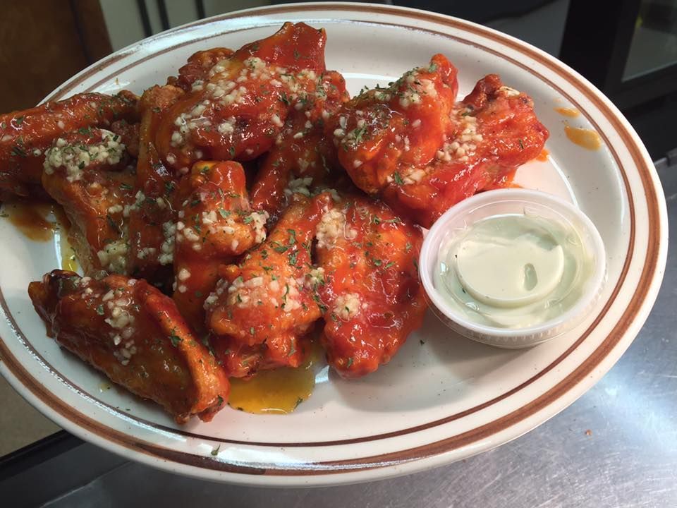 A plate of red sauce-covered chicken wings garnished with herbs and garlic, served with a side of white dipping sauce.