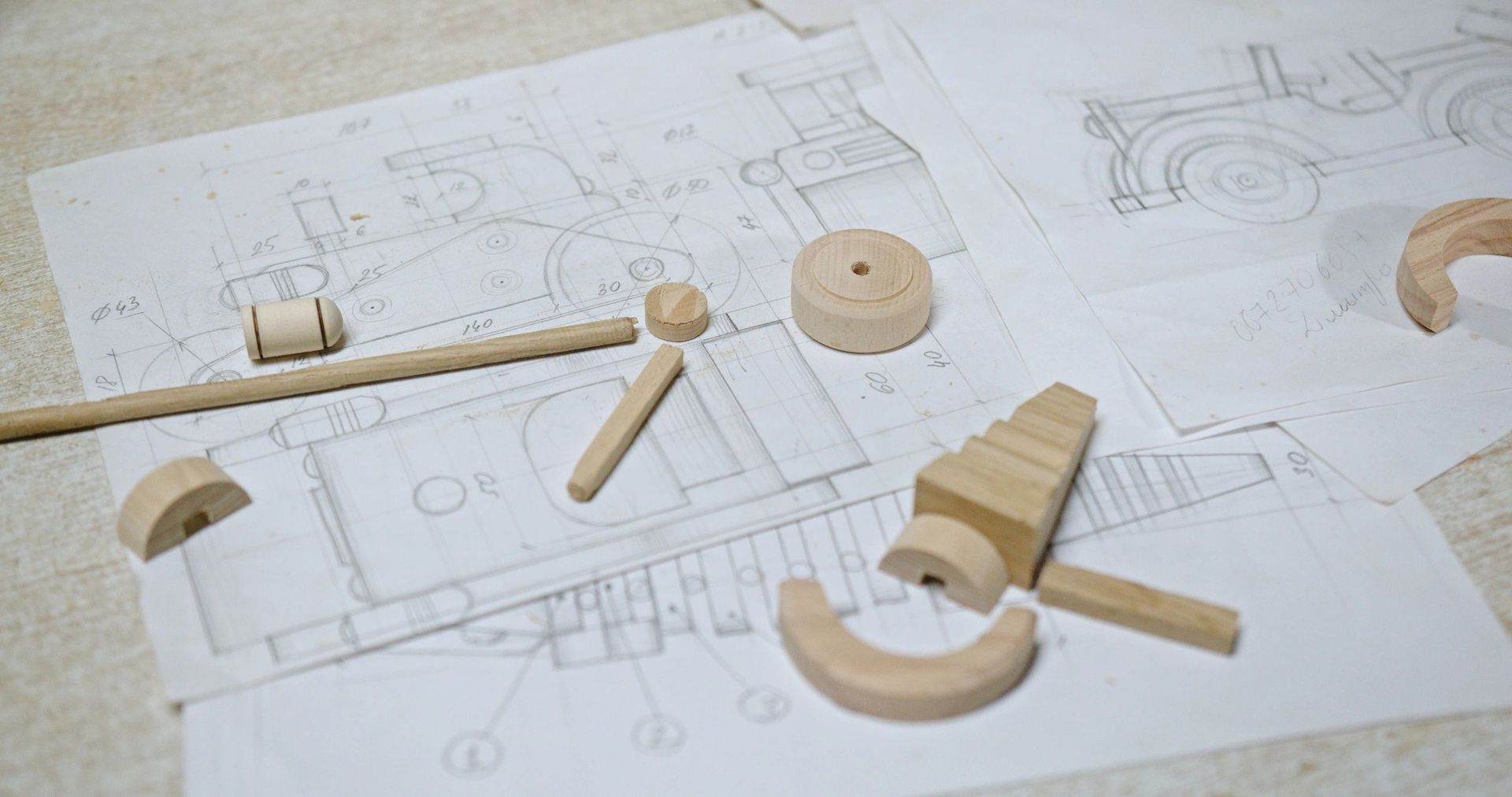 Wooden toy parts and blueprints on a white surface, suggesting a woodworking project.