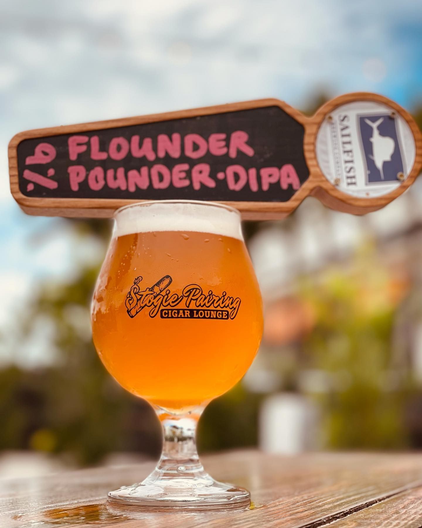 A glass of beer is sitting on a table next to a sign that says flounder pounder-dipa