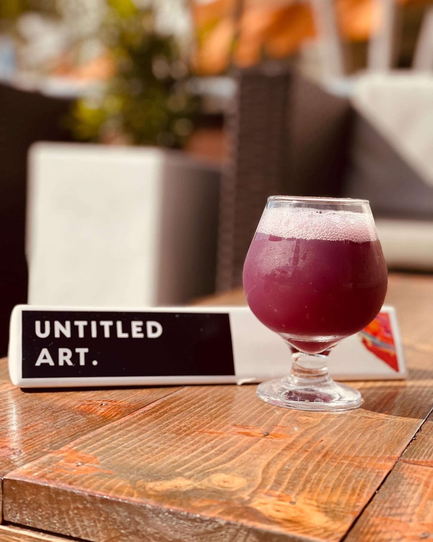 A glass of purple liquid next to a sign that says untitled art