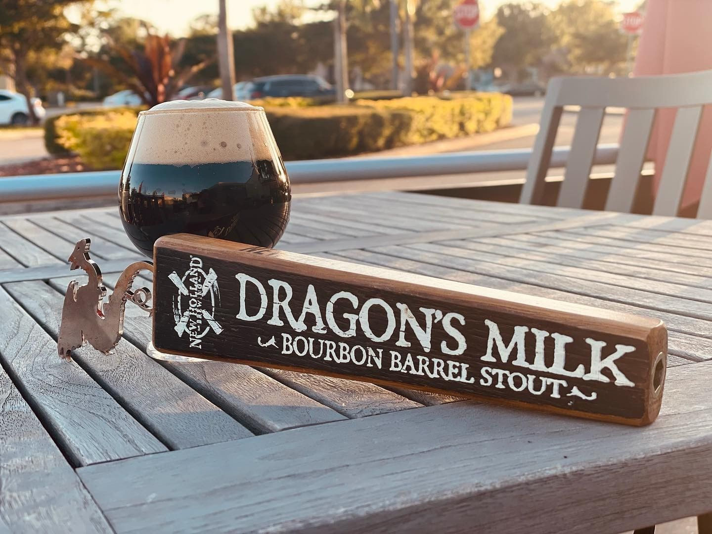 A wooden sign that says dragon 's milk is on a table next to a glass of beer.