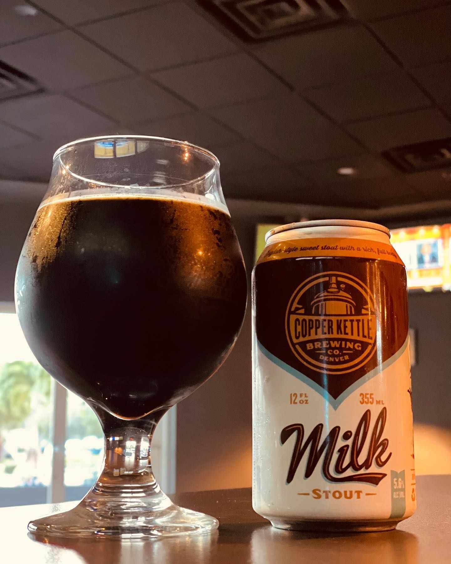 A glass of beer next to a can of milk stout