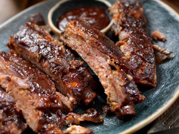 Barbecued ribs with dark brown glaze on blue plate, dipping sauce.