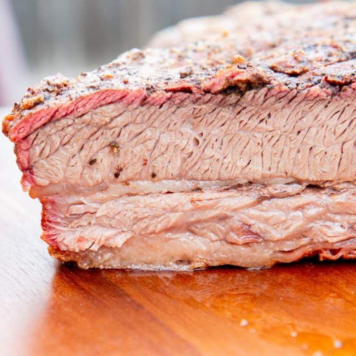 Close-up of a sliced smoked brisket with a visible pink smoke ring and fat layers on a wooden surface.
