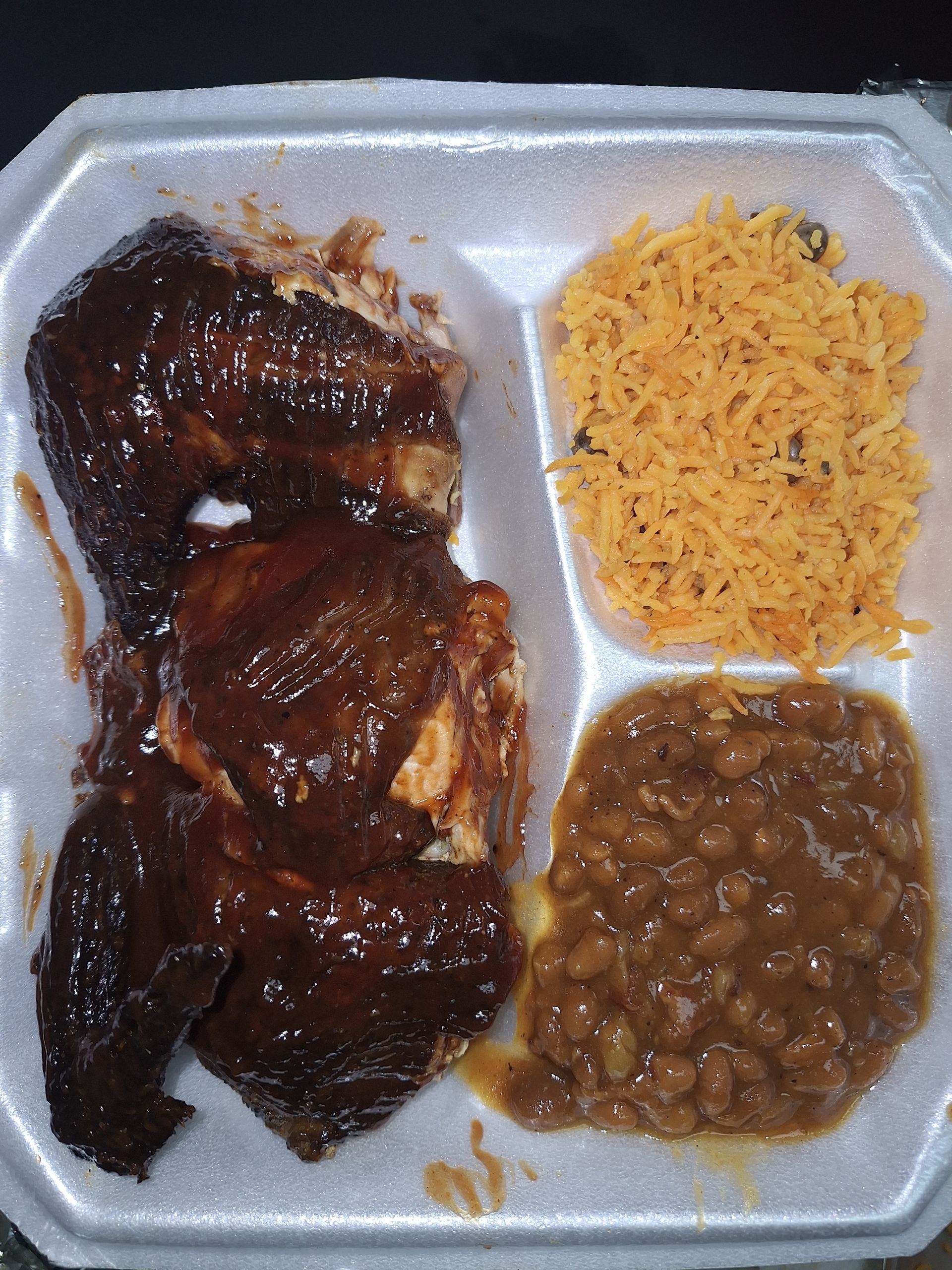 BBQ chicken meal in a foam container with yellow rice and beans.