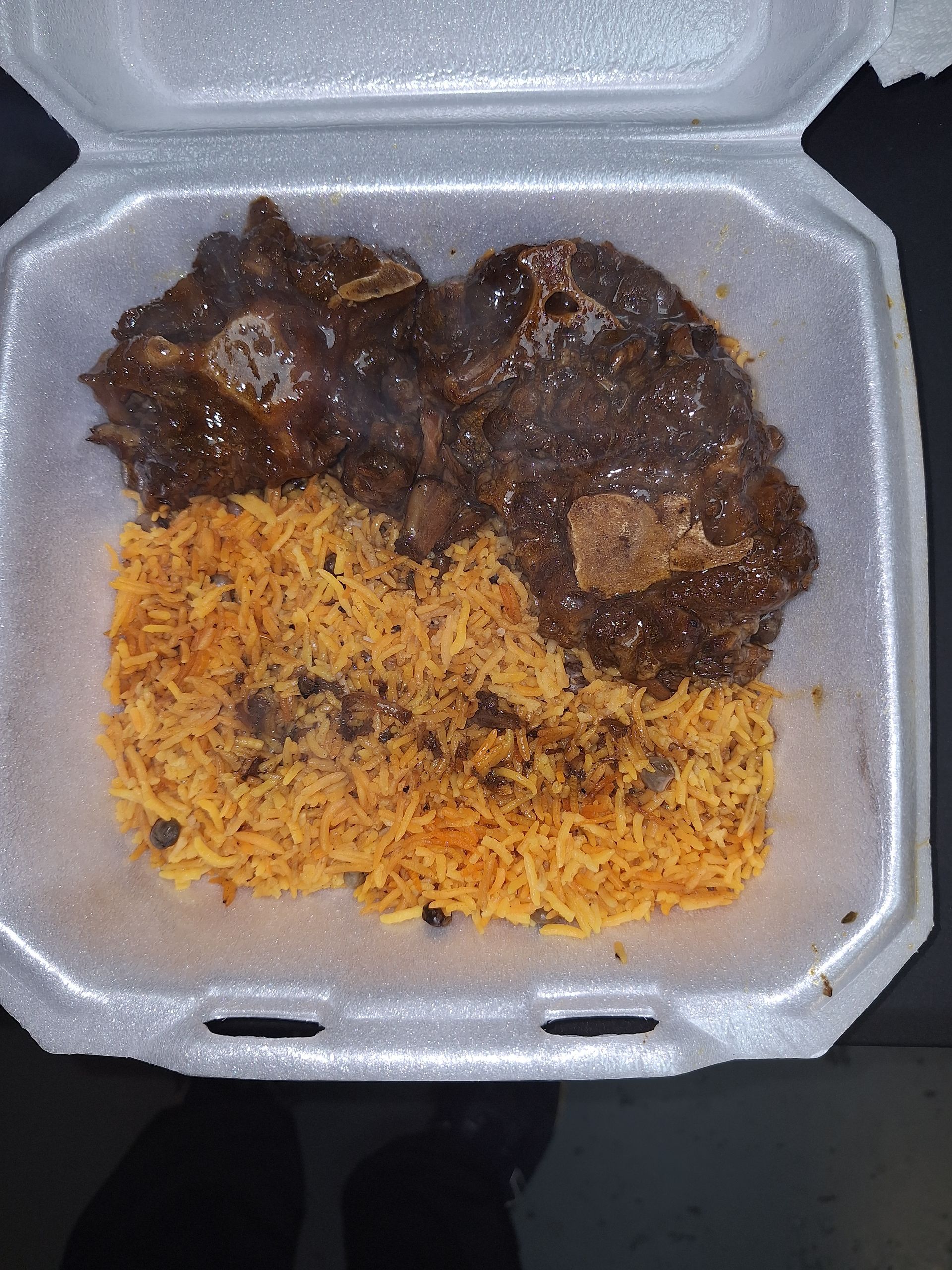 A takeout container with seasoned rice and dark meat, possibly stewed.