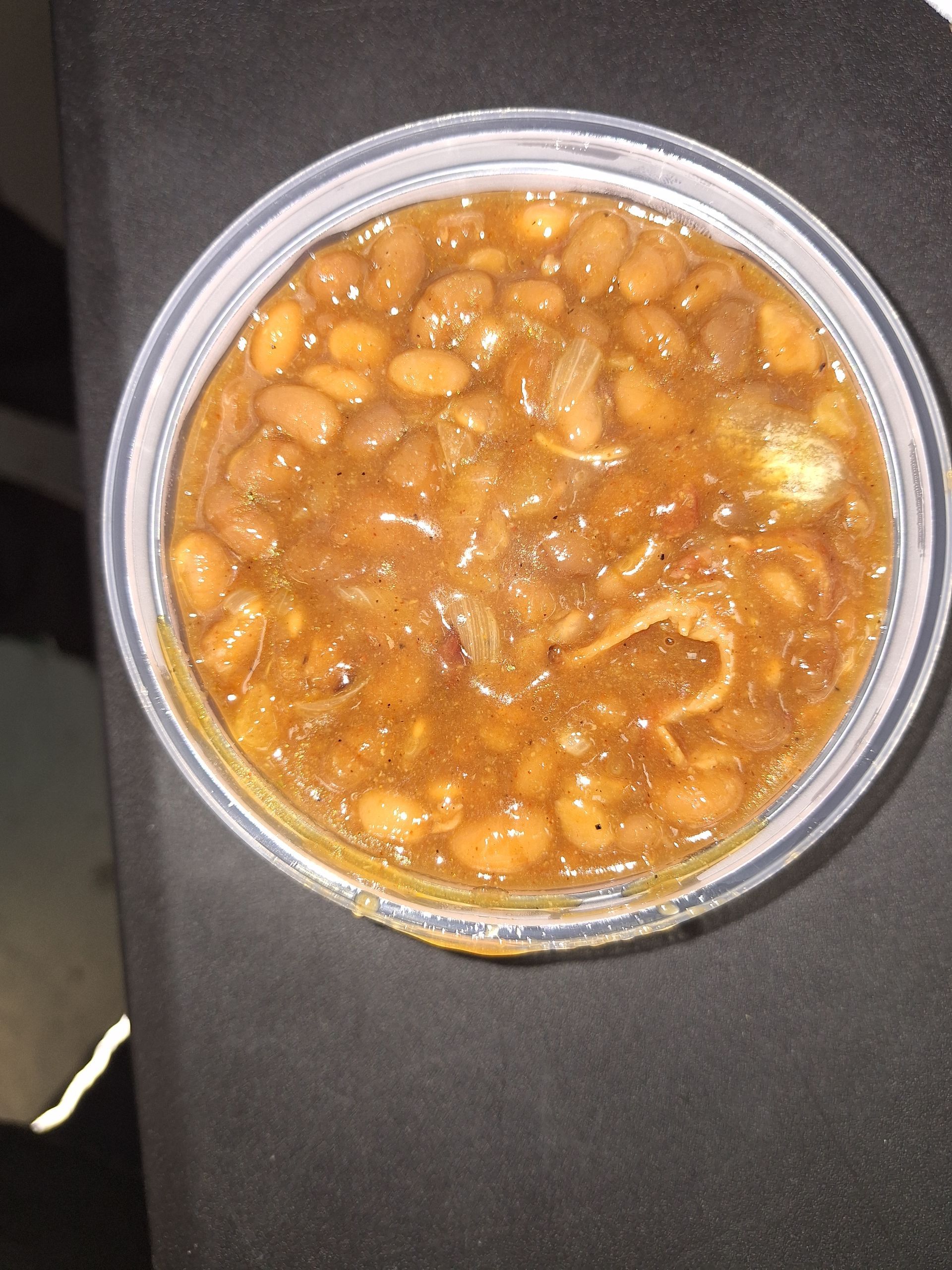 A plastic container filled with baked beans in a brownish sauce.