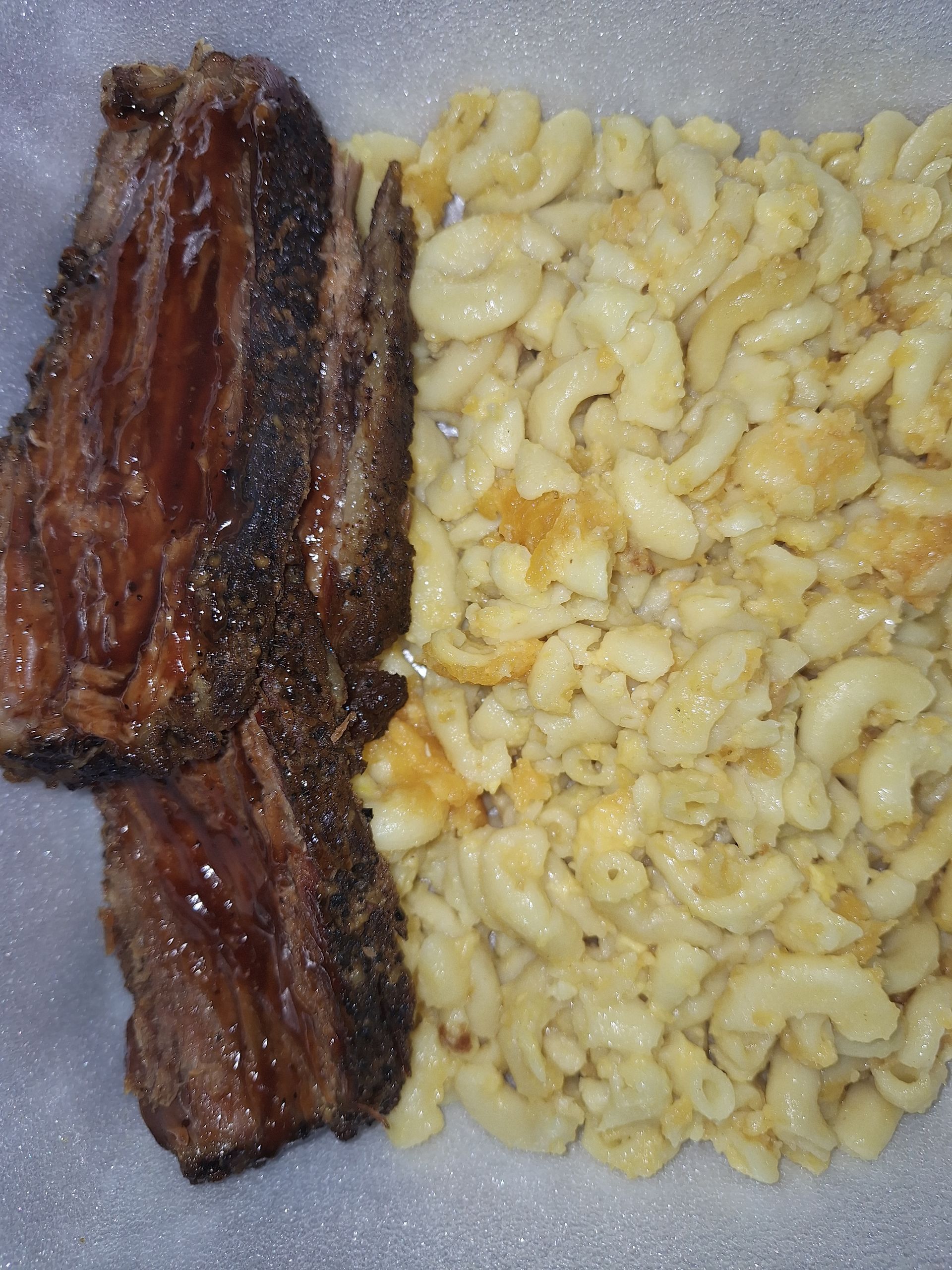 Brisket and macaroni and cheese on a white surface; the brisket is dark and the mac and cheese is creamy.