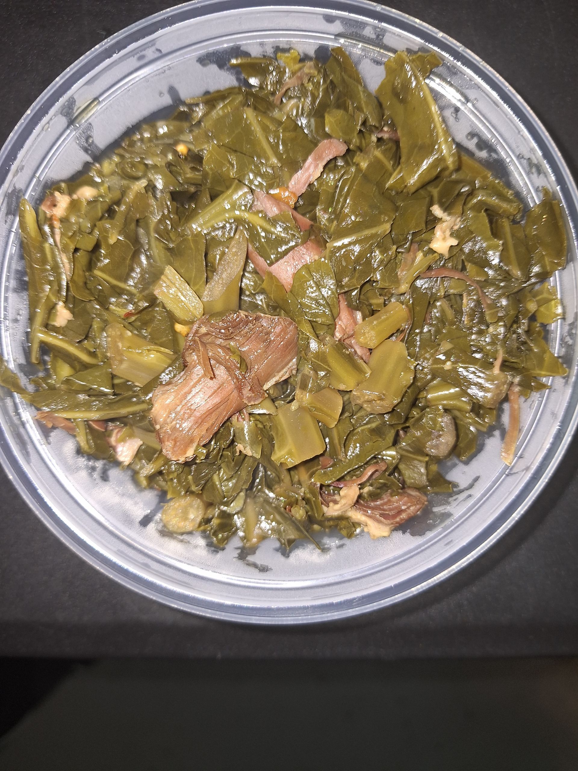 Collard greens with meat in a clear container.
