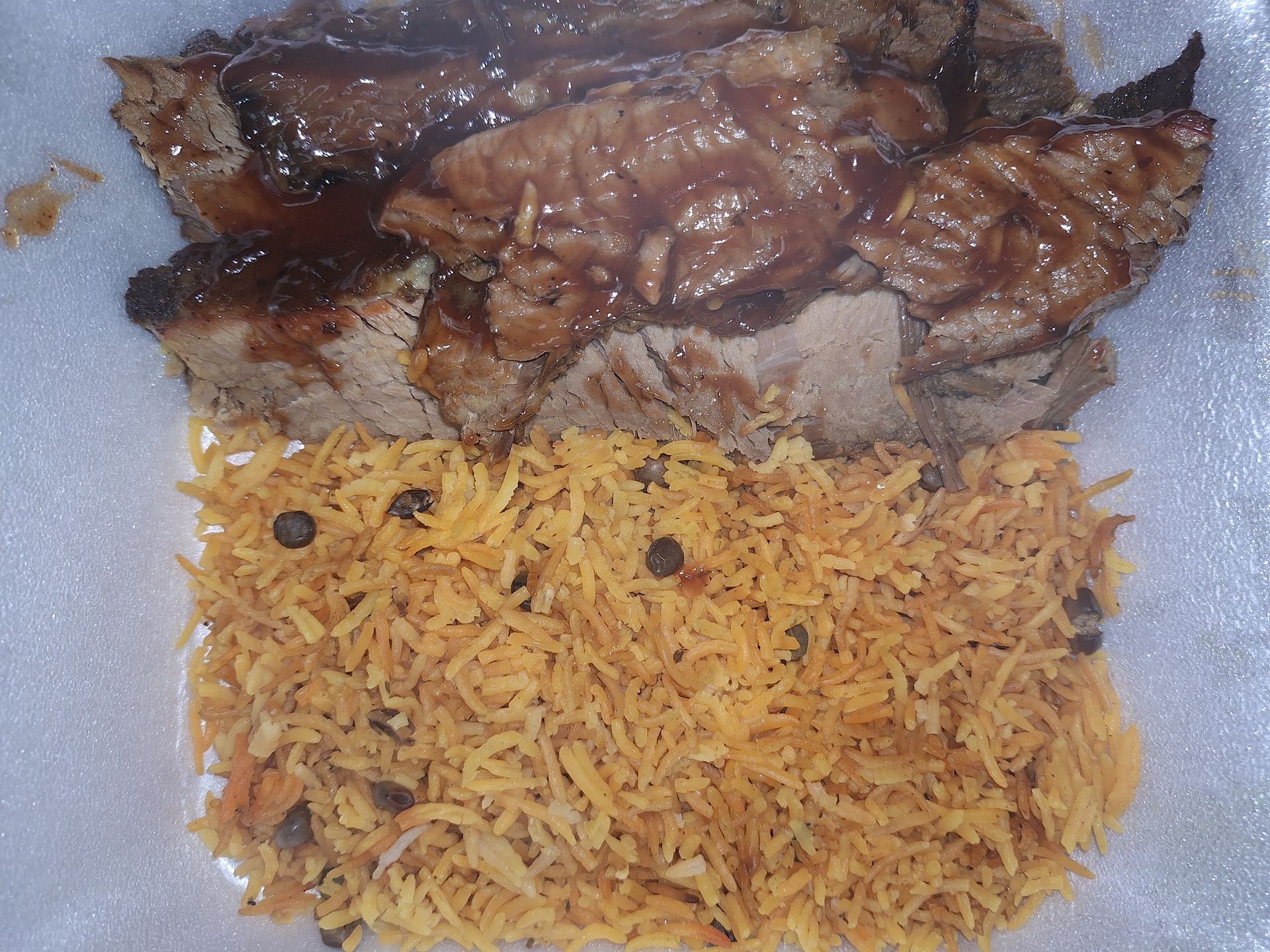 Grilled meat with brown sauce over a bed of yellow rice in a white container.