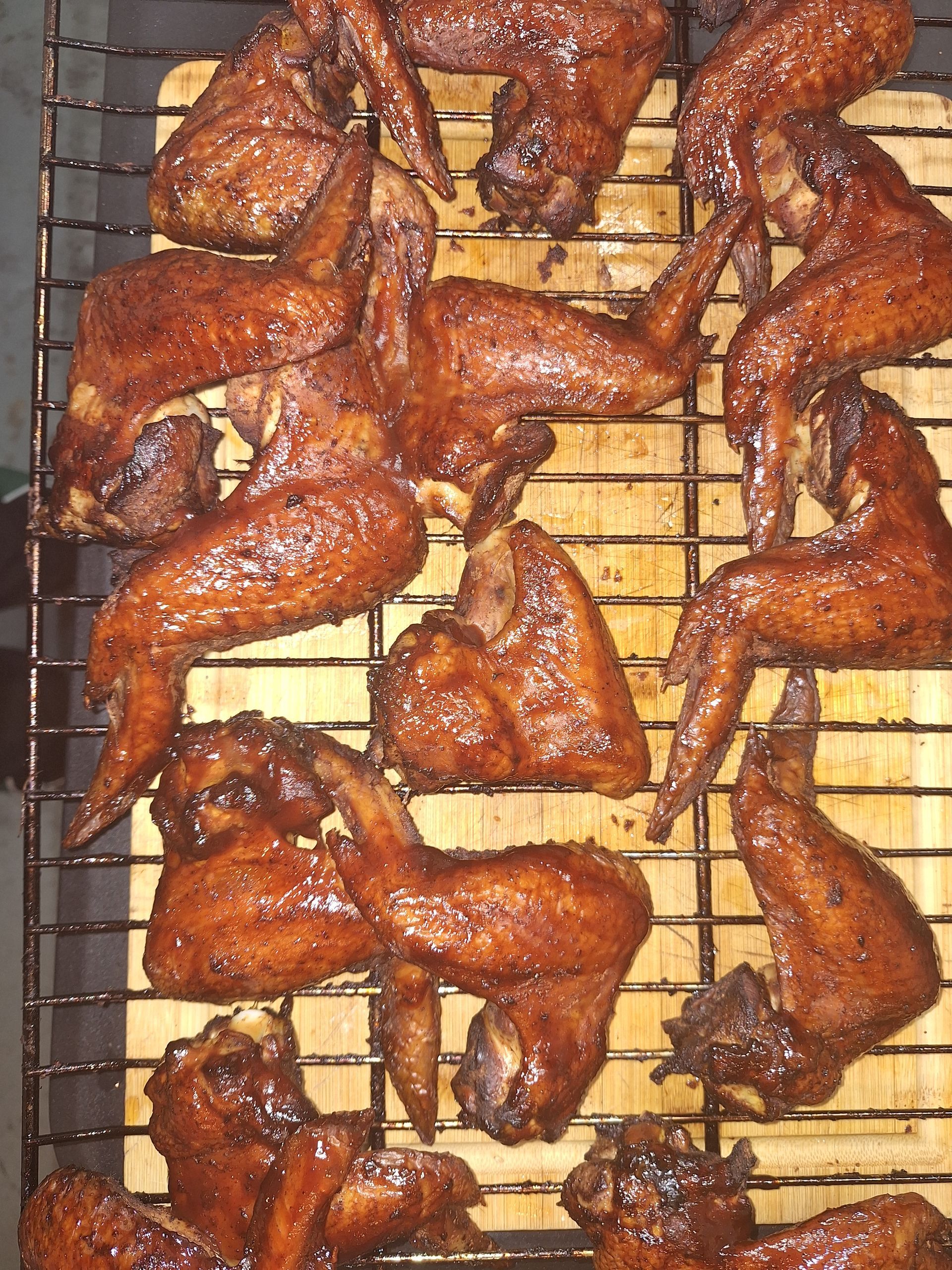 Smoked chicken wings on a wooden grate, coated in a dark, reddish-brown glaze.
