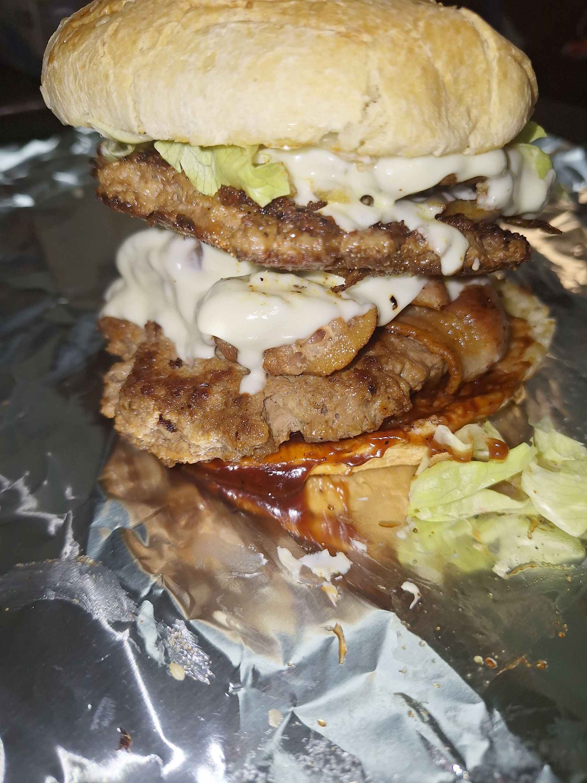 Double-decker burger on bun with sauce, lettuce, and foil wrapping.