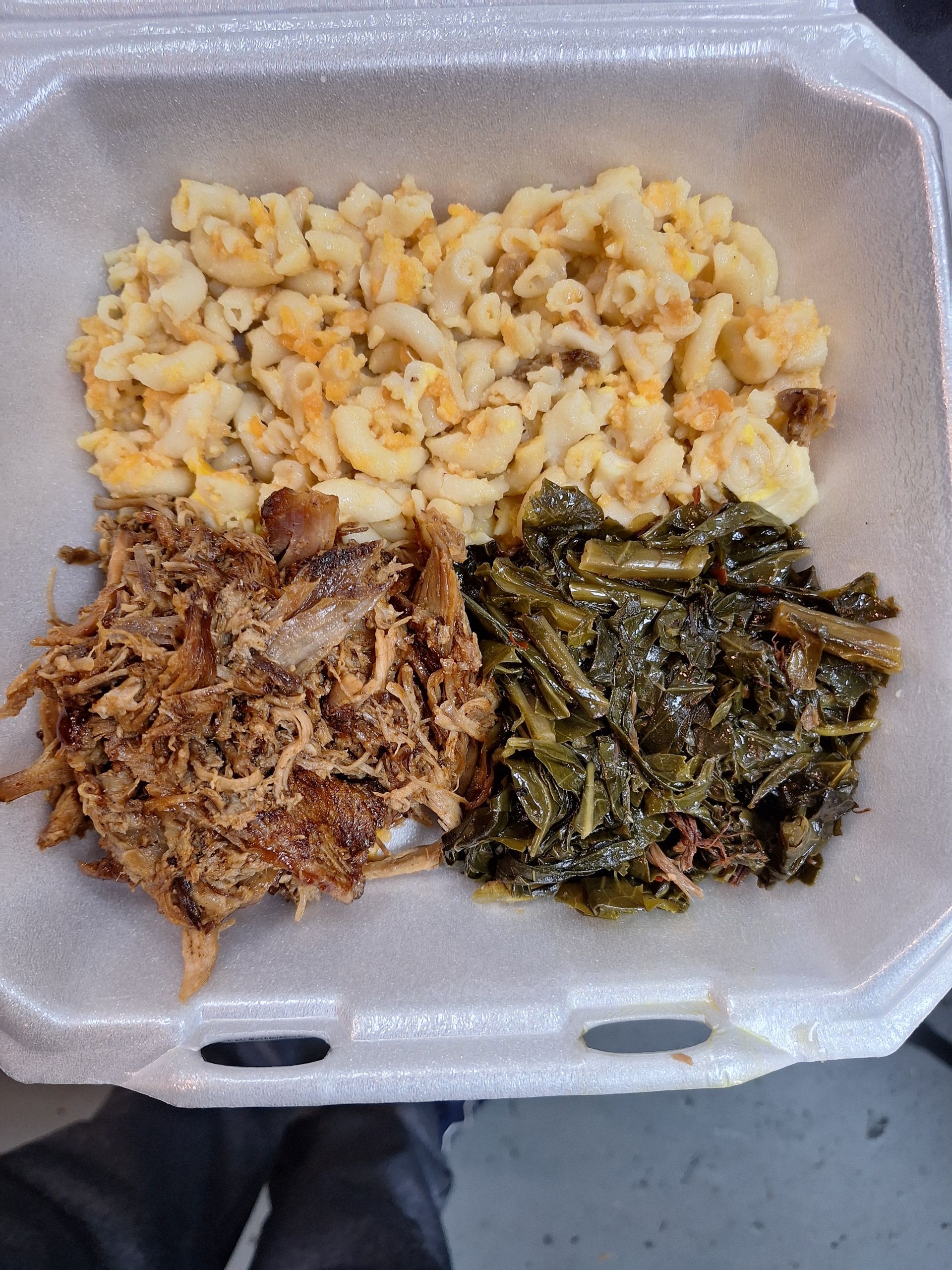 Pulled pork, mac and cheese, and collard greens in a foam container.
