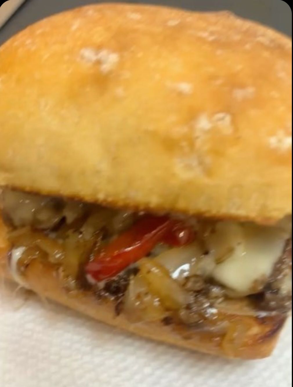 Cheesesteak sandwich on a roll with sautéed onions, peppers, and melted cheese.