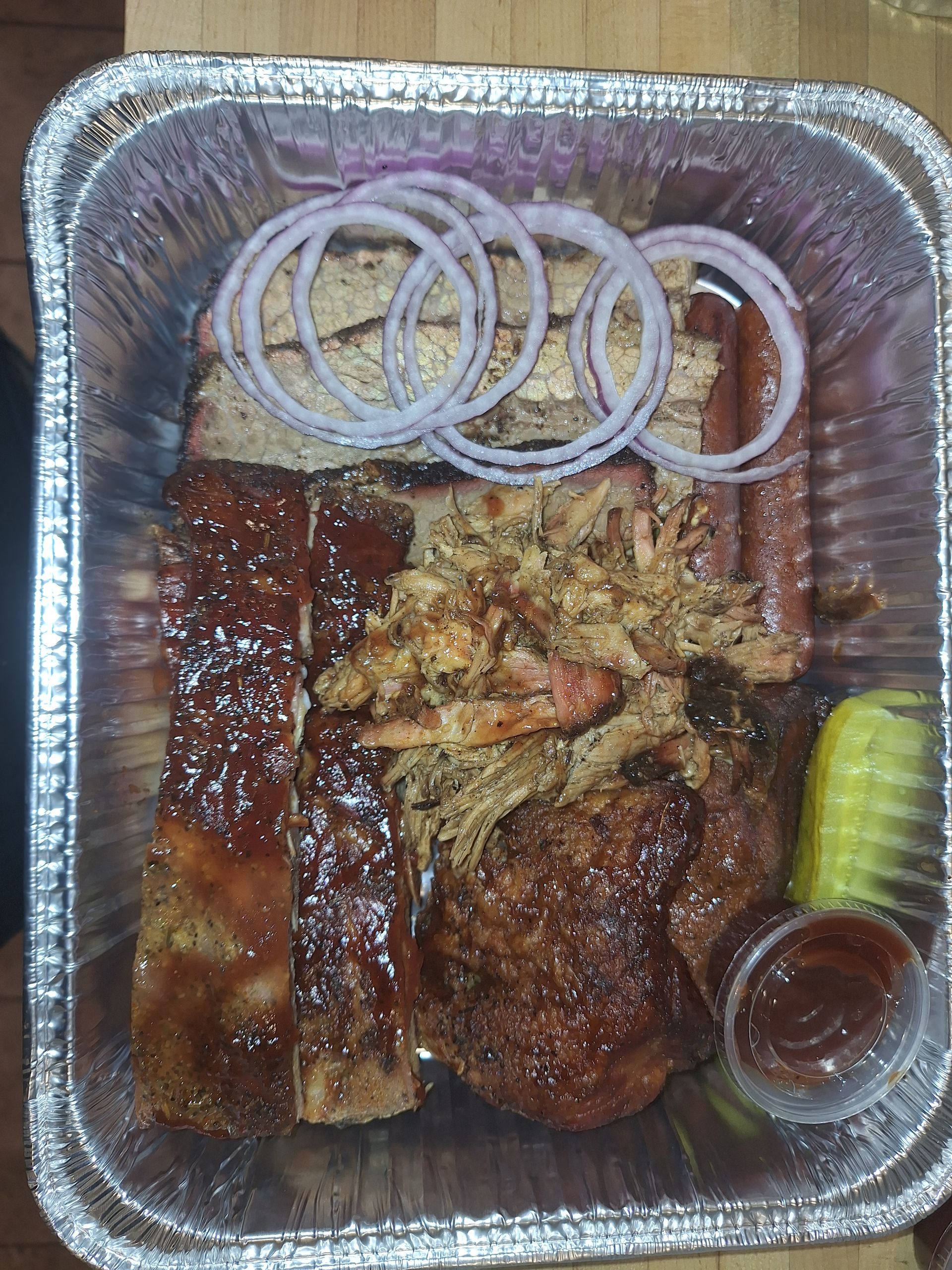 BBQ tray with ribs, pulled pork, sausage, onion rings, pickles, and sauce.