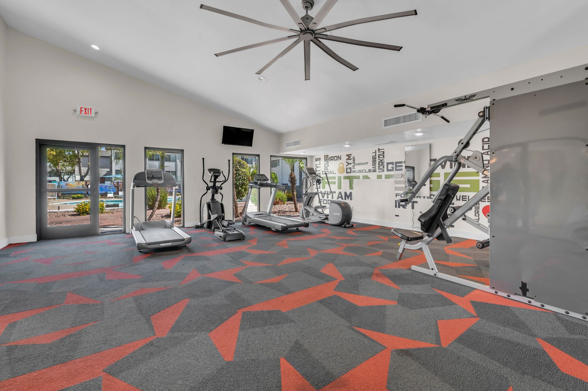 A gym with treadmills , exercise bikes , and a ceiling fan.