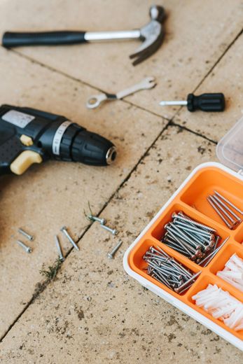 Tools and hardware: drill, hammer, screws, wrench, screwdriver, and organizer on a tiled surface.