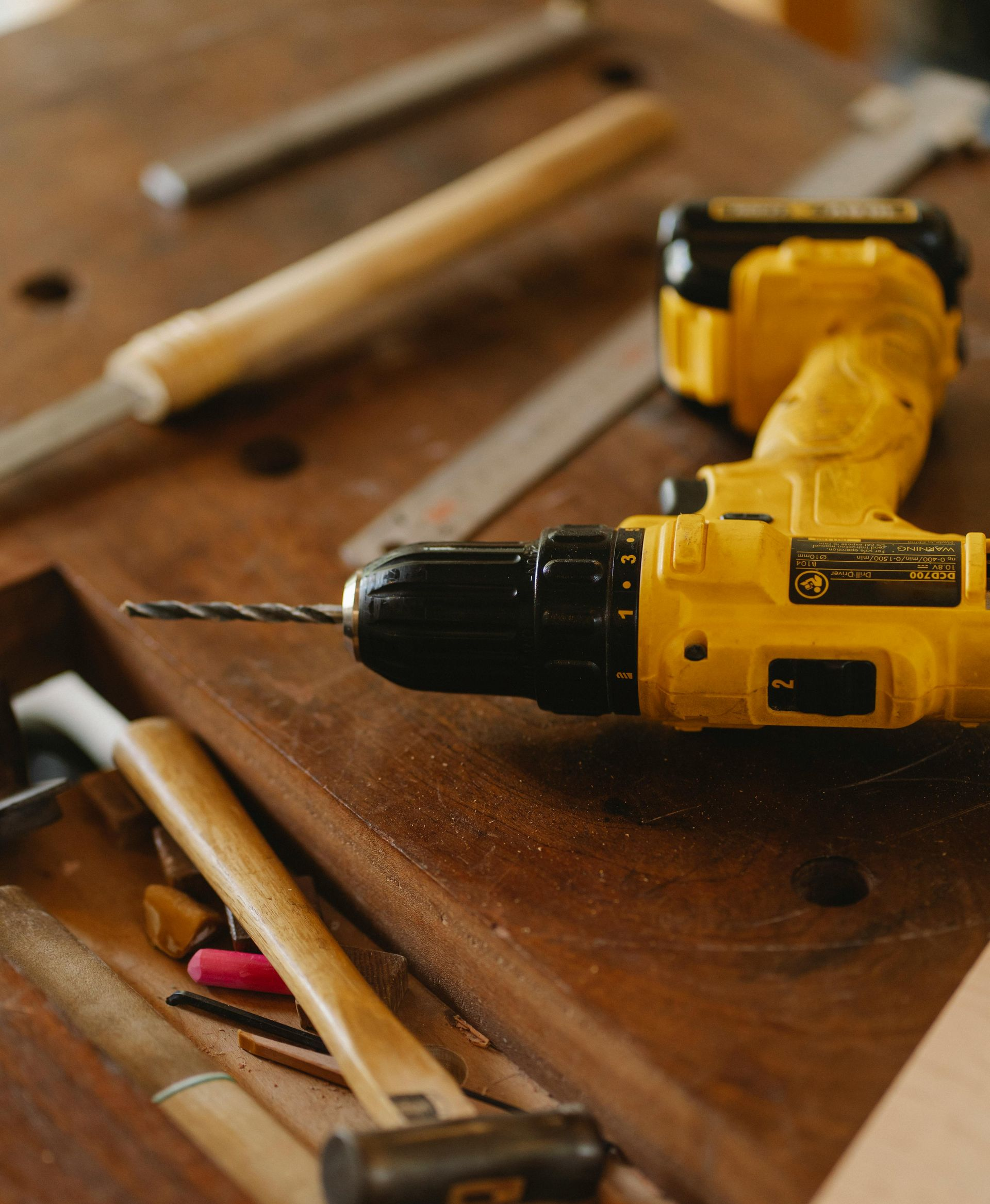 Yellow drill on a wood workbench with other tools; chisels, mallets, and measuring tools.
