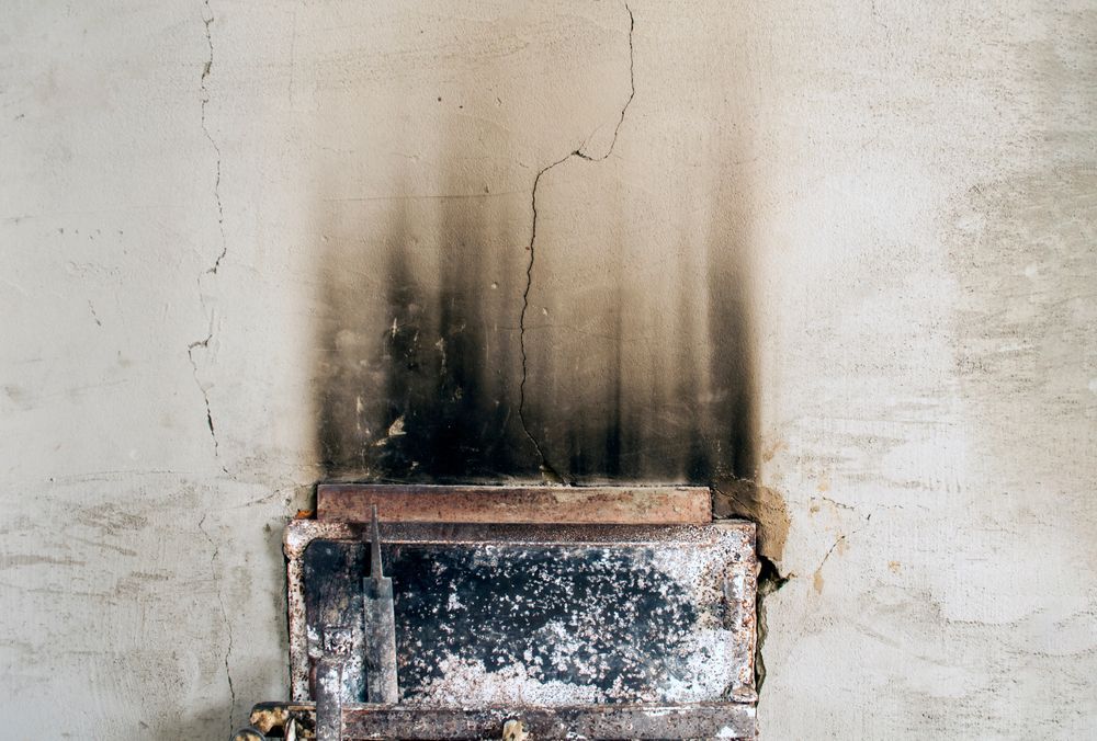 Old, soot-stained fireplace in a weathered wall, with vertical dark smudges above.