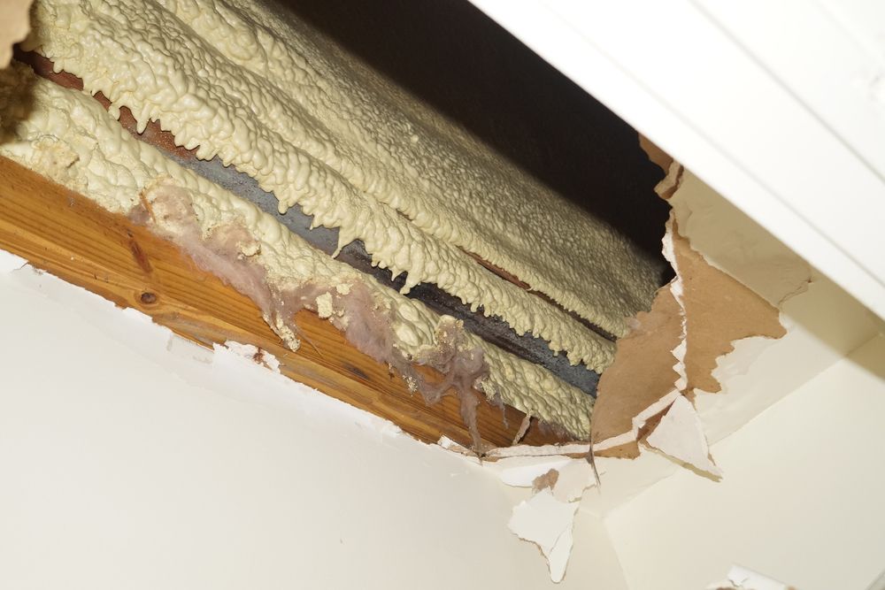 Hole in ceiling reveals insulation, with damaged drywall and liquid dripping, interior shot.