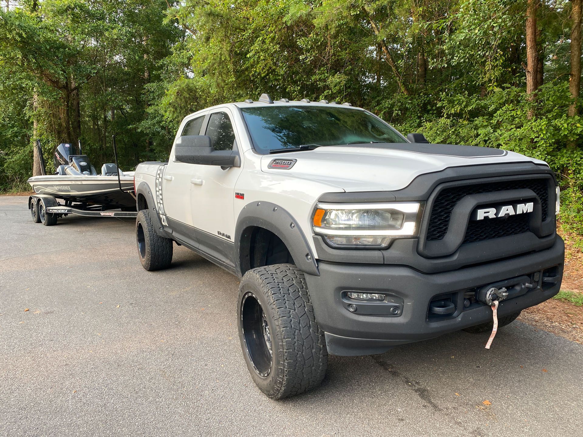 A white ram truck is towing a boat on a trailer.