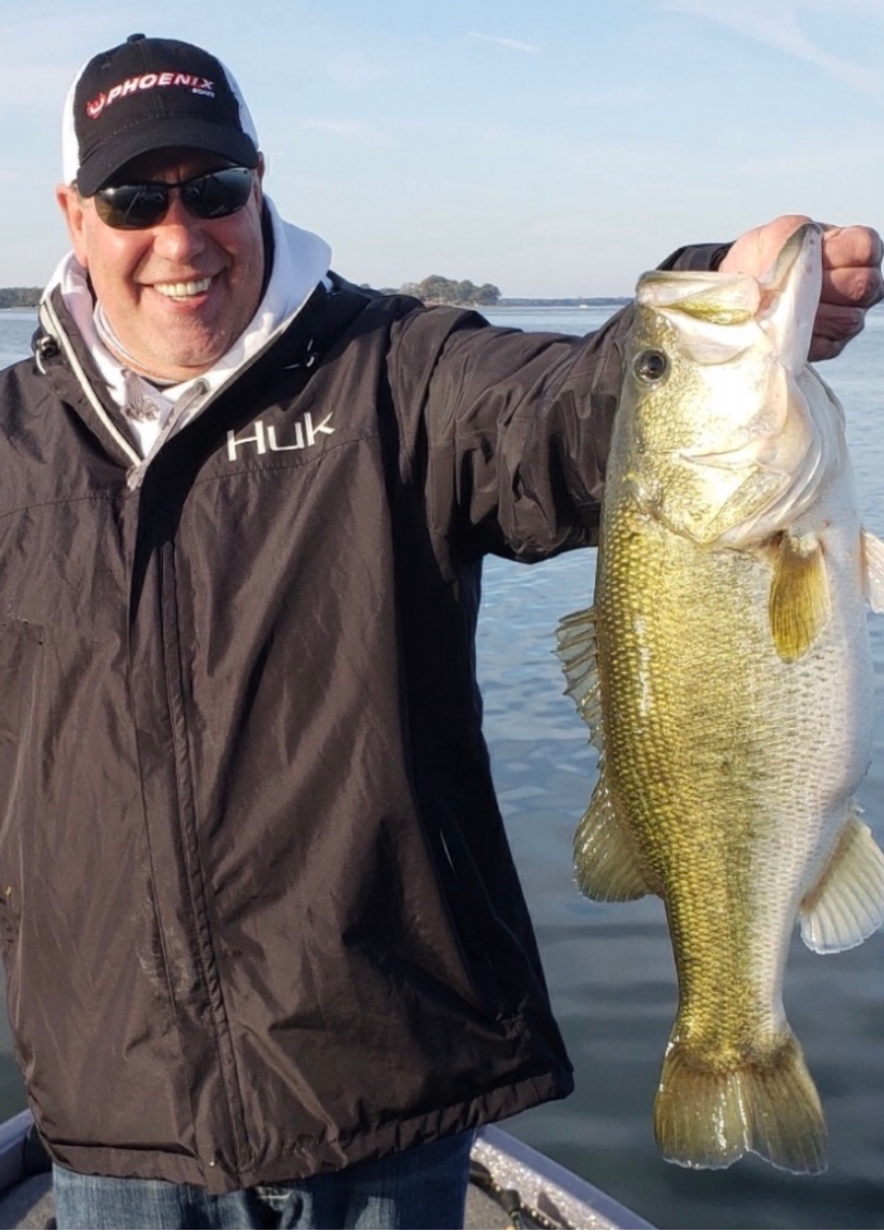 A man wearing a jacket that says huk is holding a large fish