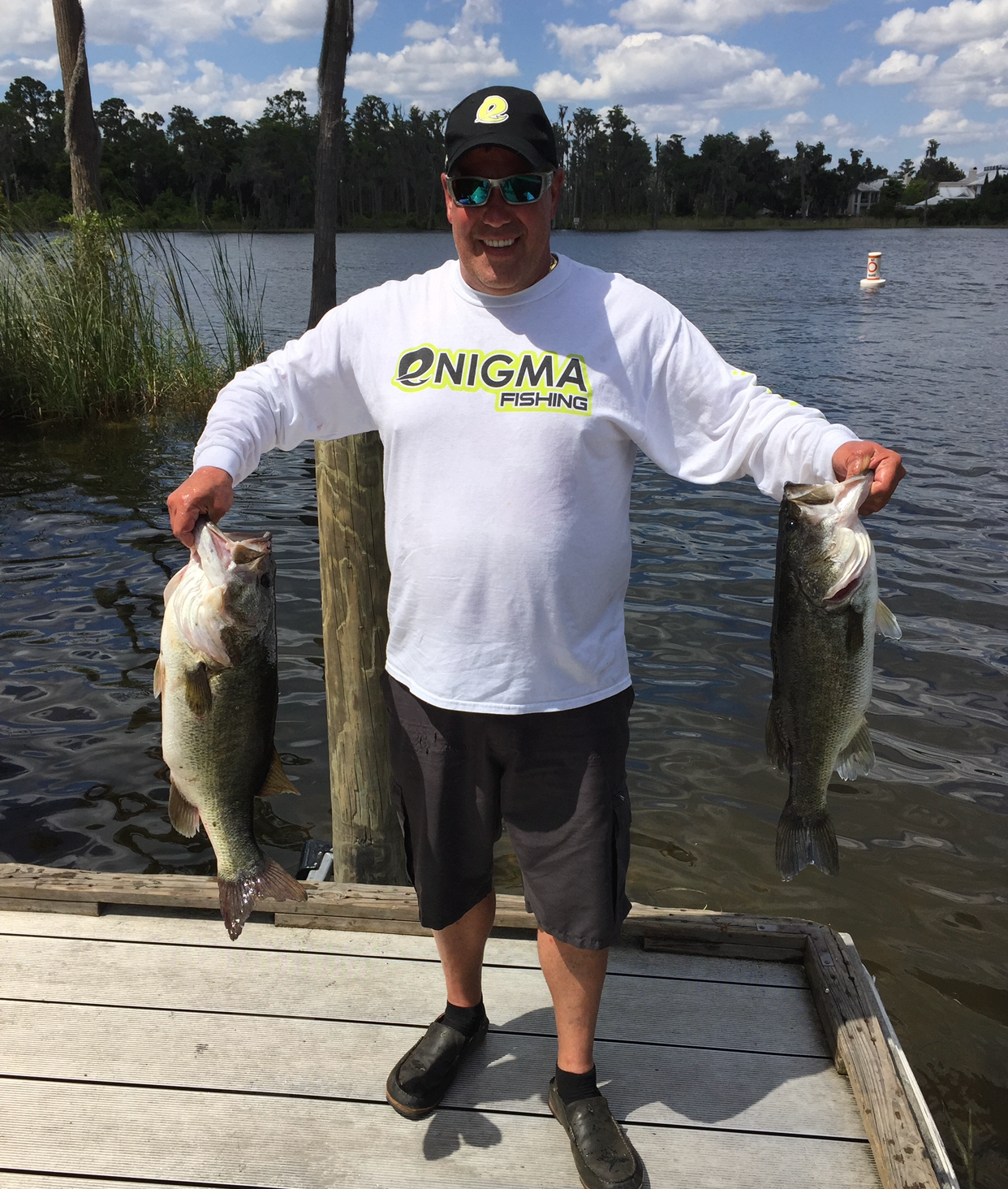 A man is standing on a dock holding two fish.