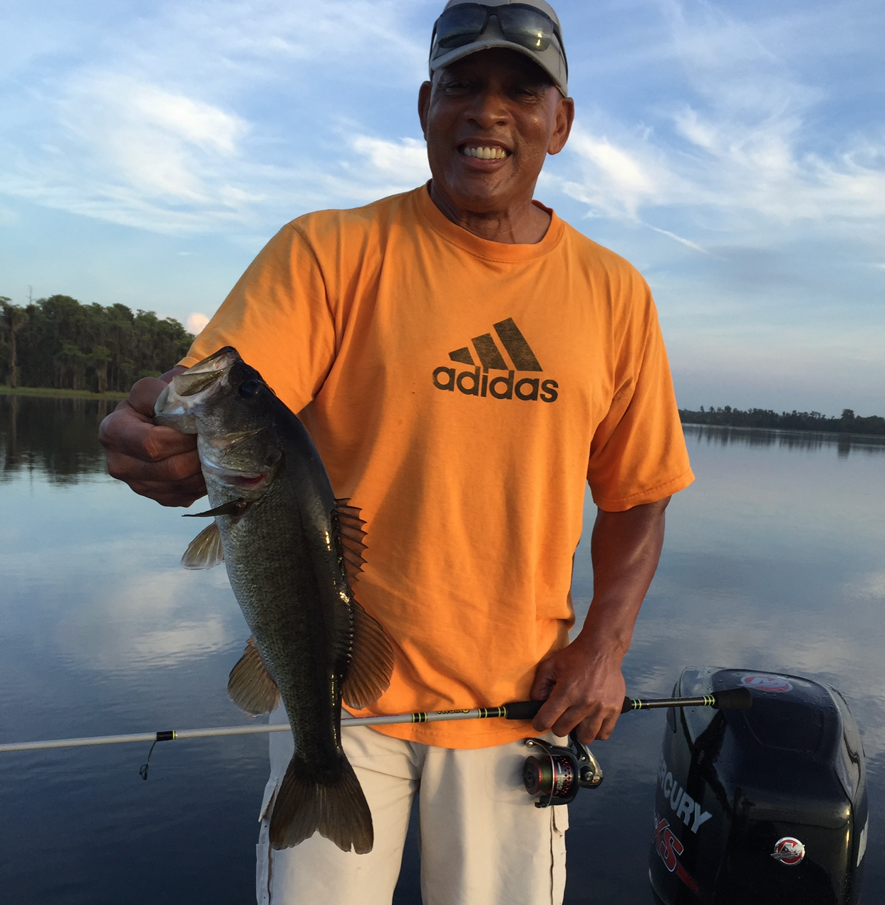 A man wearing an orange adidas shirt is holding a large fish