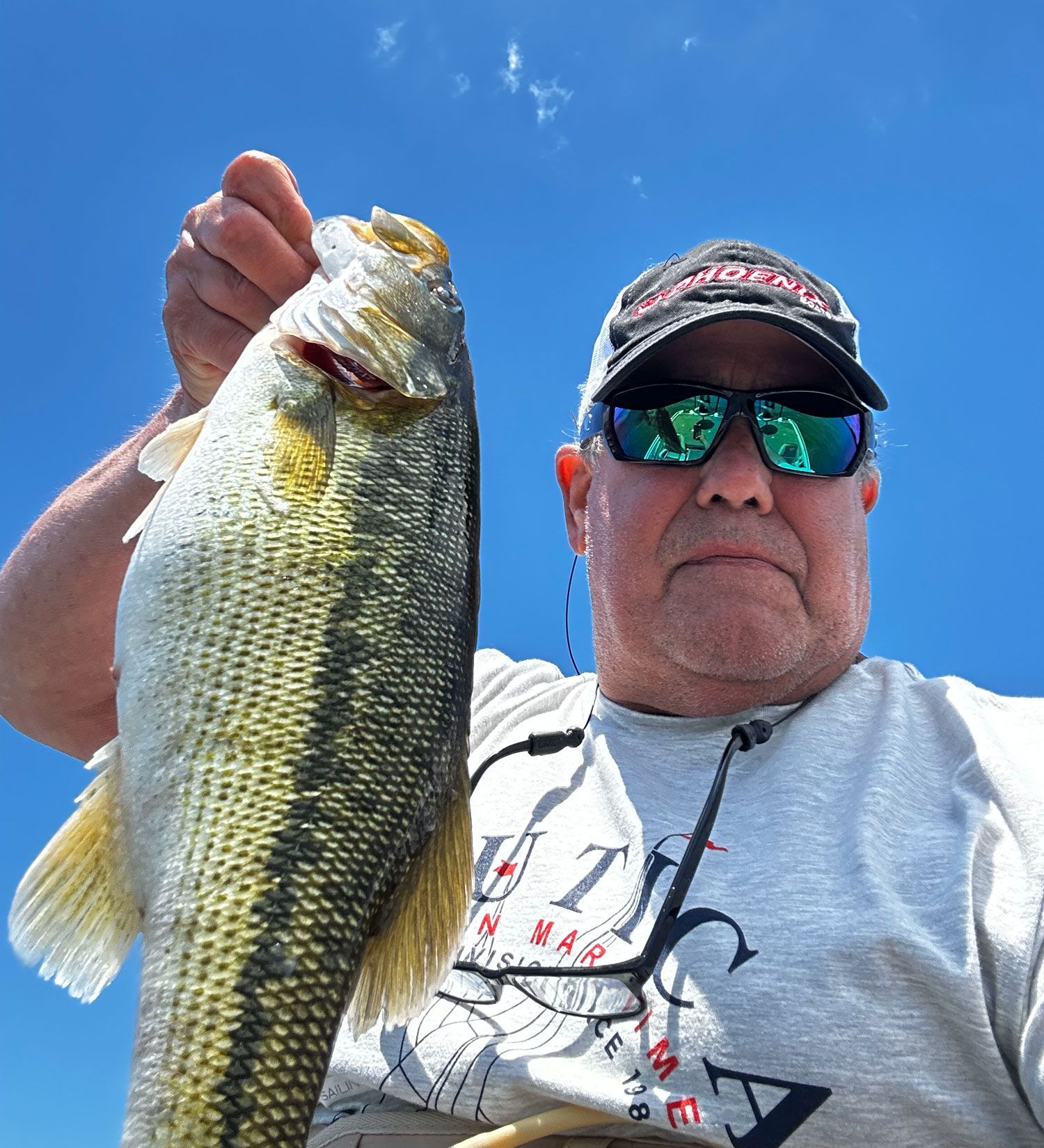 A man wearing sunglasses and a hat is holding a large fish in his hands.