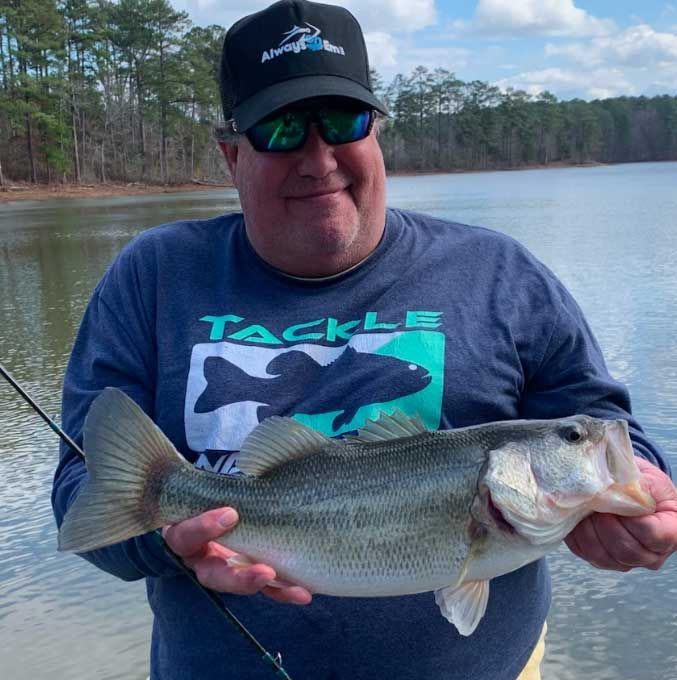 A man wearing a tackle shirt is holding a large fish