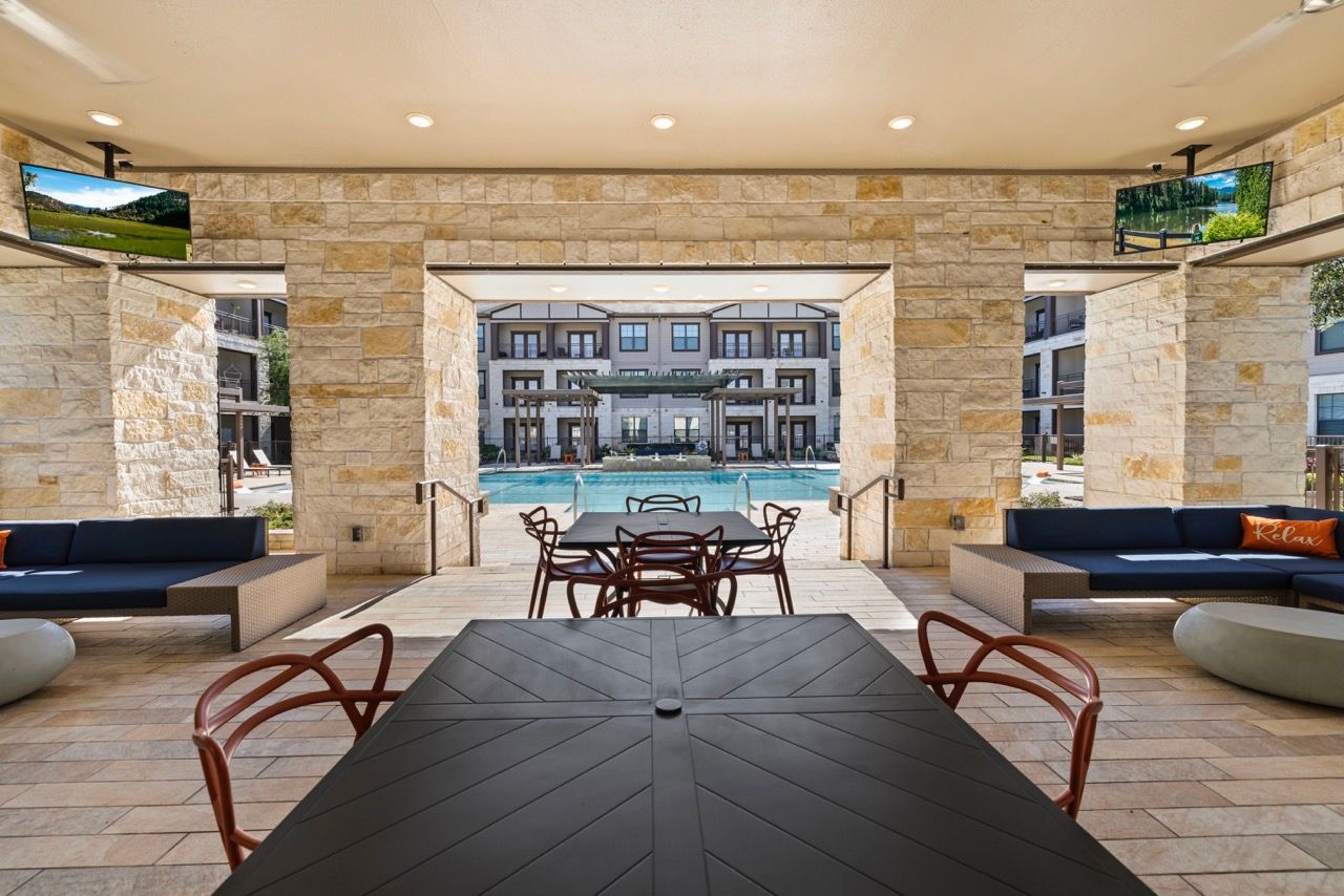 Covered outdoor lounge with tables and seating facing a resort-style pool.