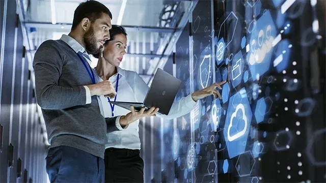 A man and a woman are looking at a laptop in a server room.
