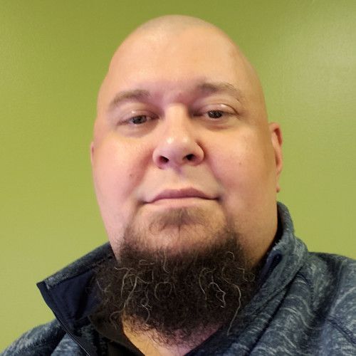 A bald man with a beard is wearing a blue jacket.