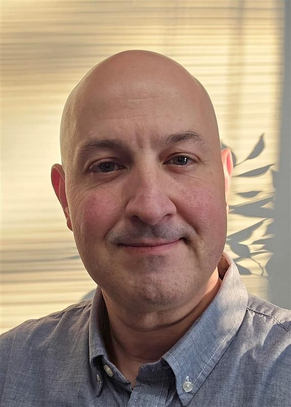 A bald man in a blue shirt is smiling for the camera.