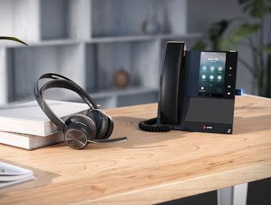 A phone and headphones are sitting on a wooden desk.