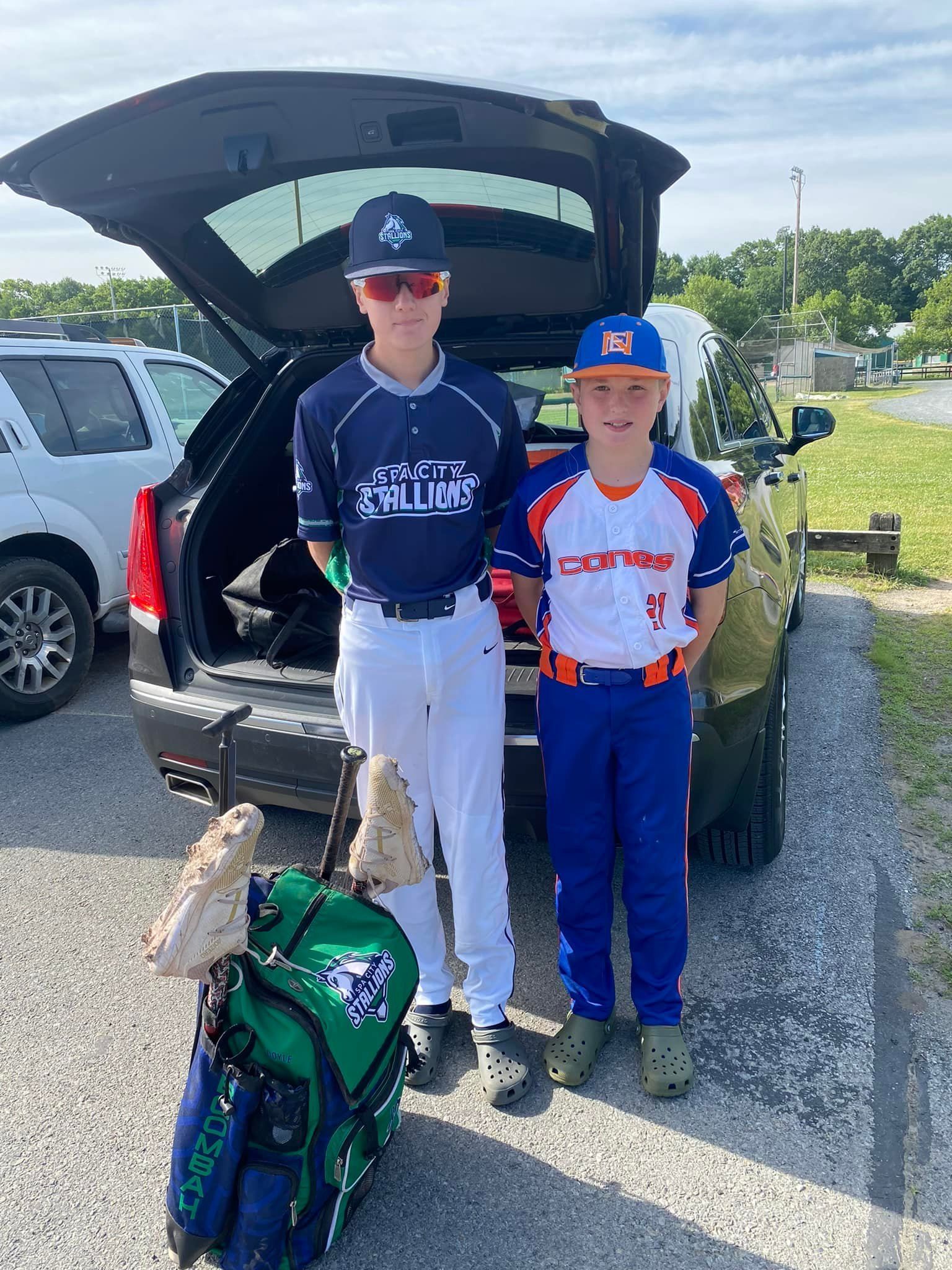 Two young boys are standing next to each other in front of a car.