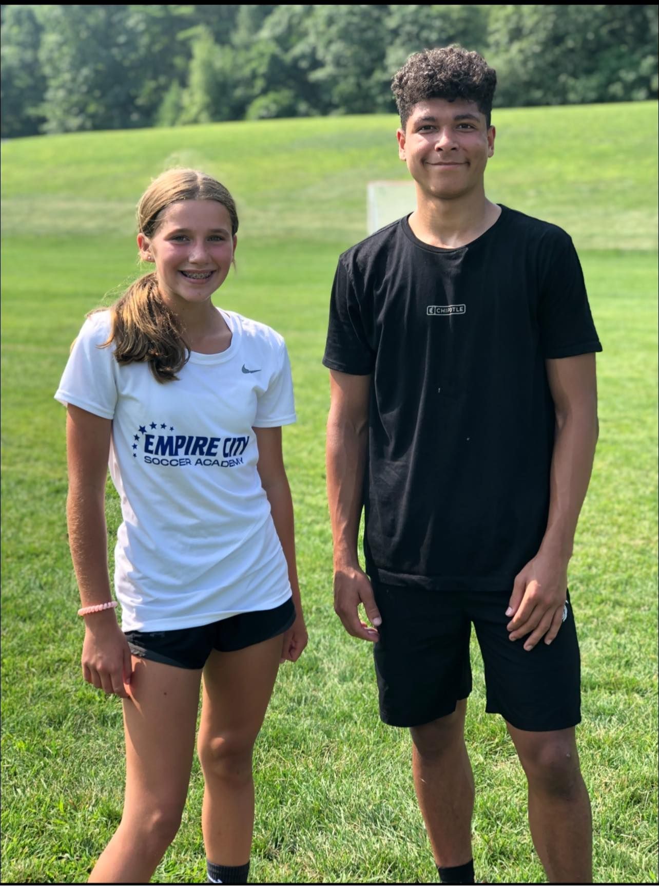 A boy and a girl are standing next to each other in a field.