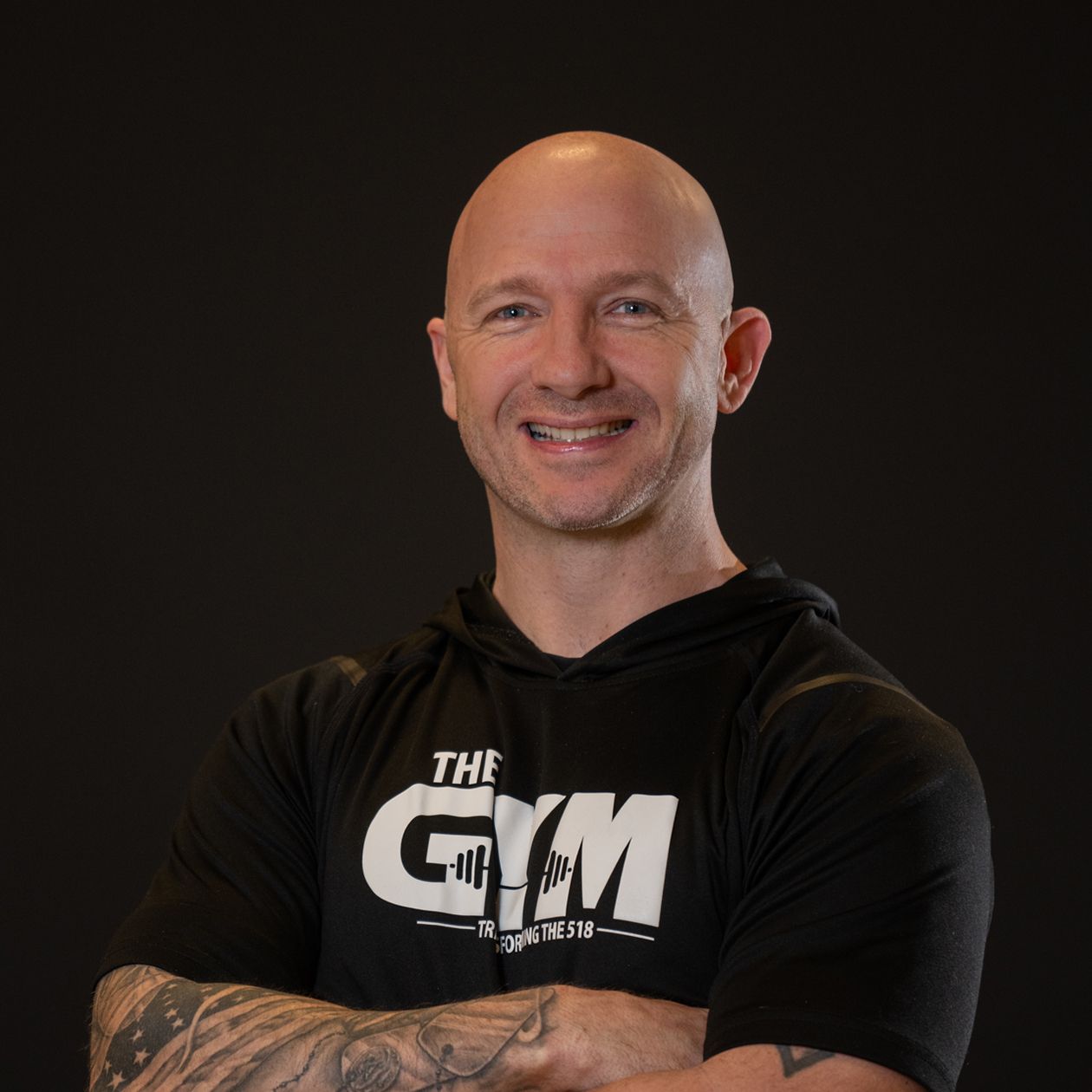 Bald man smiling, wearing a black hooded shirt with