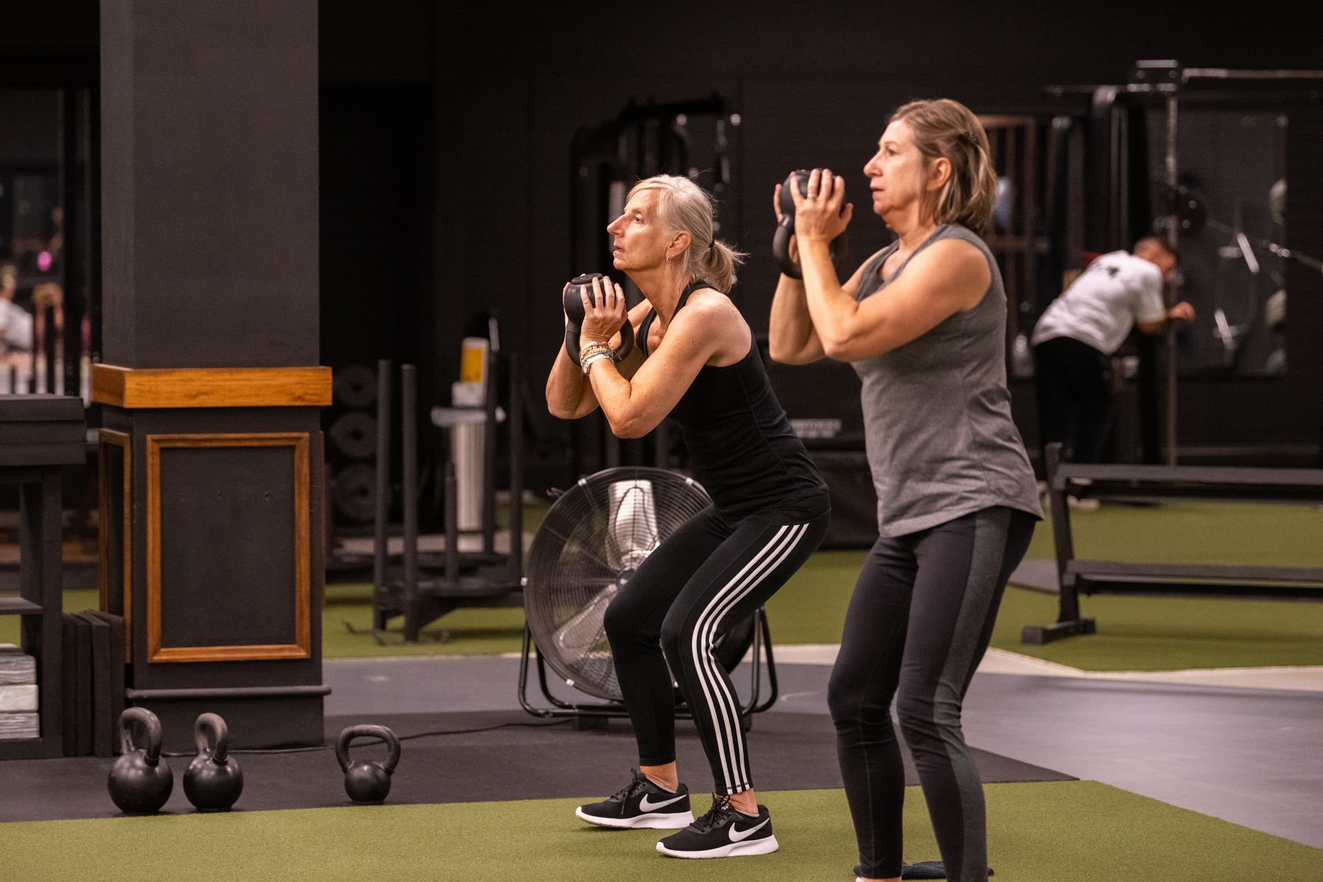 Two women are doing squats in a gym.