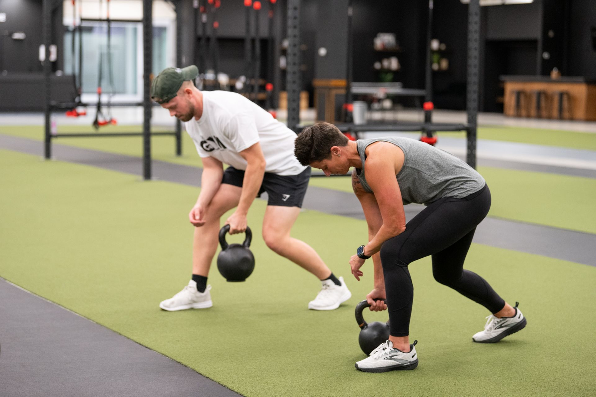 A man and a woman are lifting kettlebells in a gym.