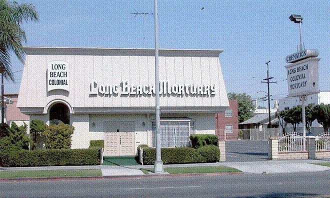 Long Beach Mortuary building with sign, trimmed hedges, and palm trees on a sunny day.