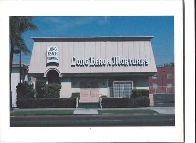 Long Beach Mortuary building with sign. Cream-colored exterior, trimmed hedges, and palm tree in the background.