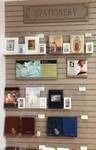 Stationery display with framed art, cards, and notebooks on a slat wall. Wooden sign above reads “Stationery.”