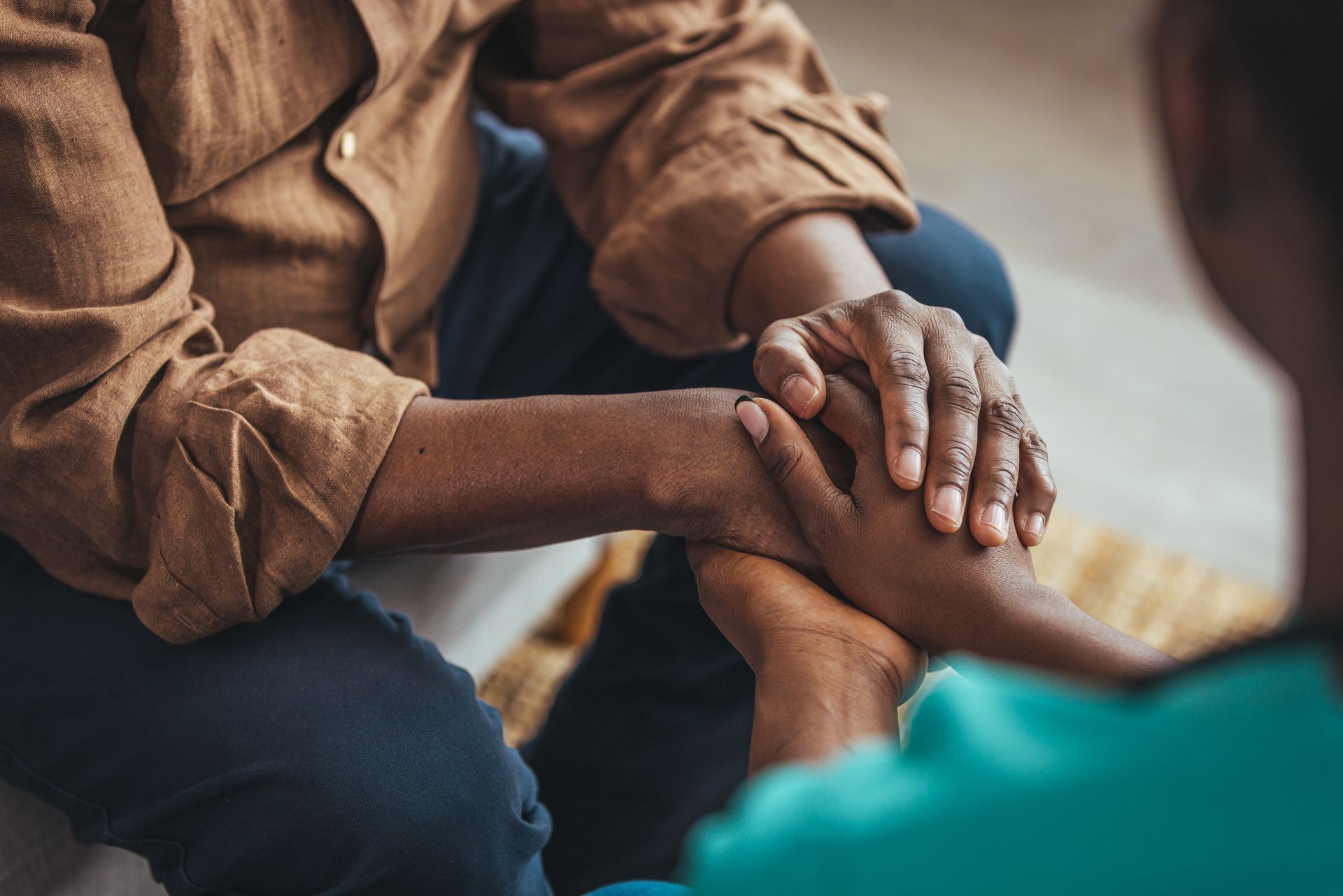 Hands clasped on a wooden table, suggesting comfort or support. One wrist has a watch.