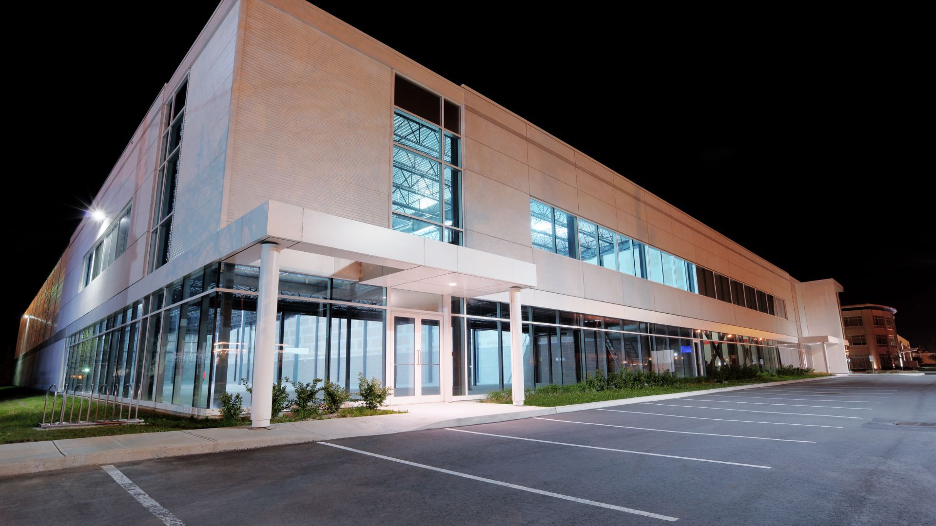 A multi-story commercial building with a glass facade and parking lot at night.