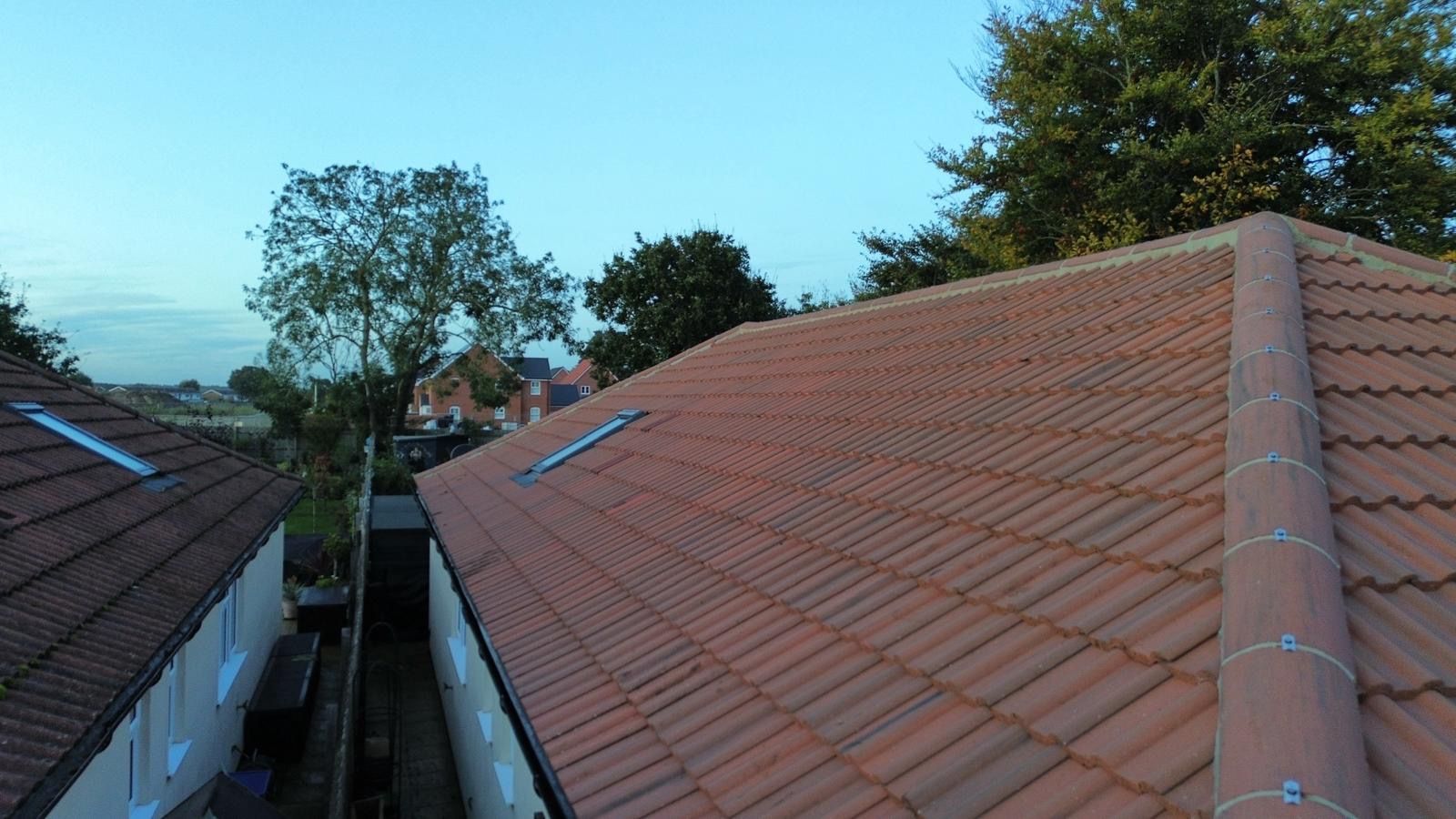 Red-tiled rooftops of two houses, with a view of trees and a blue sky in the background.