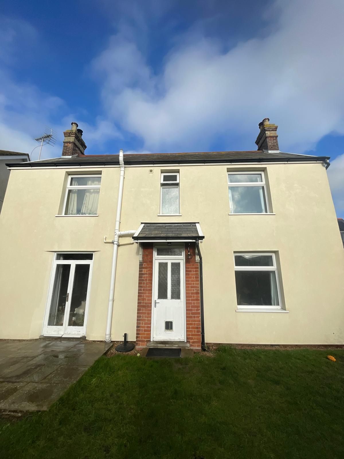 Two-story beige house with white windows and door, brick doorway under a gray awning. Green lawn. Blue sky.