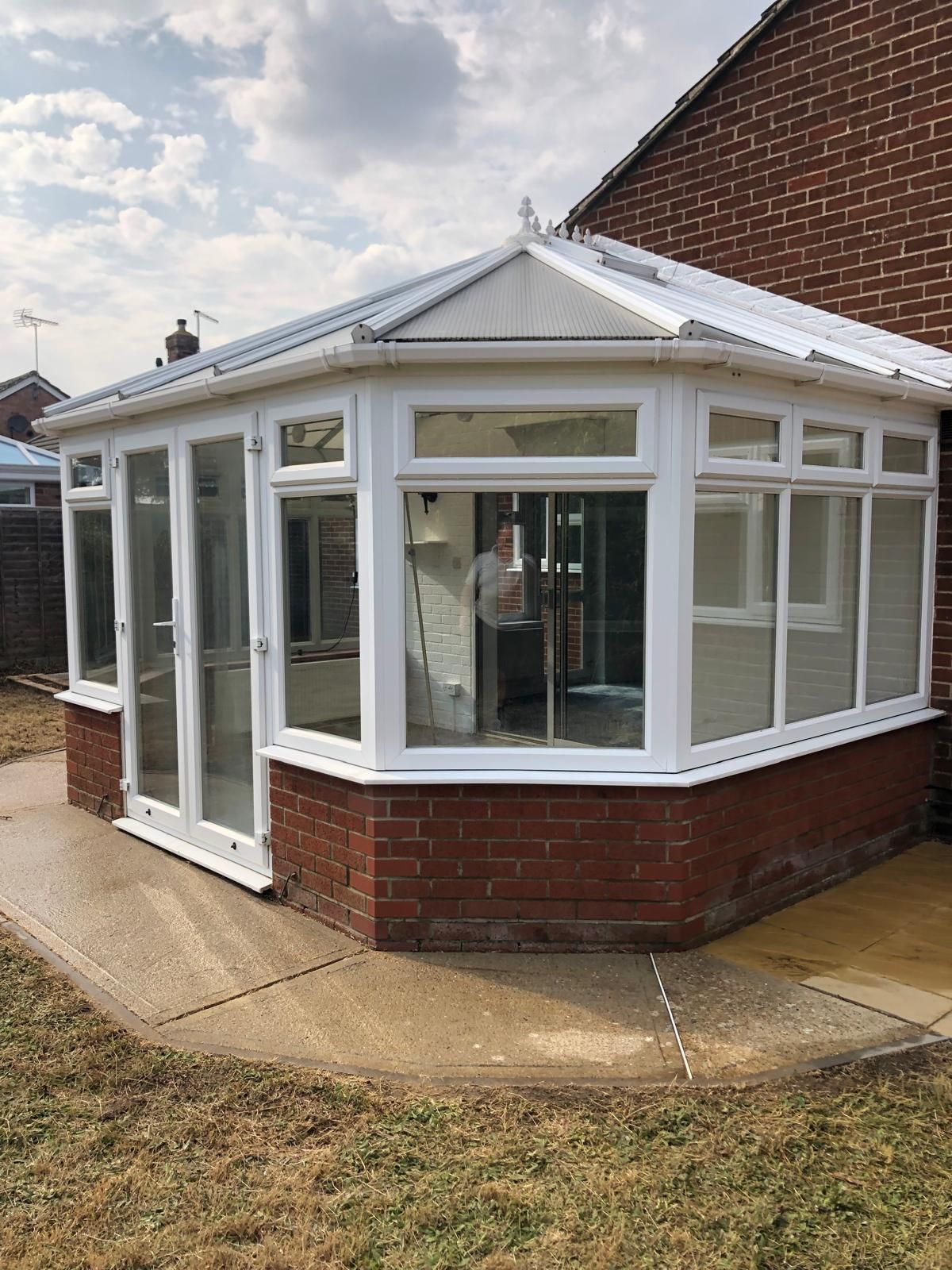 White-framed conservatory with a brick base and glass windows, attached to a red brick house.